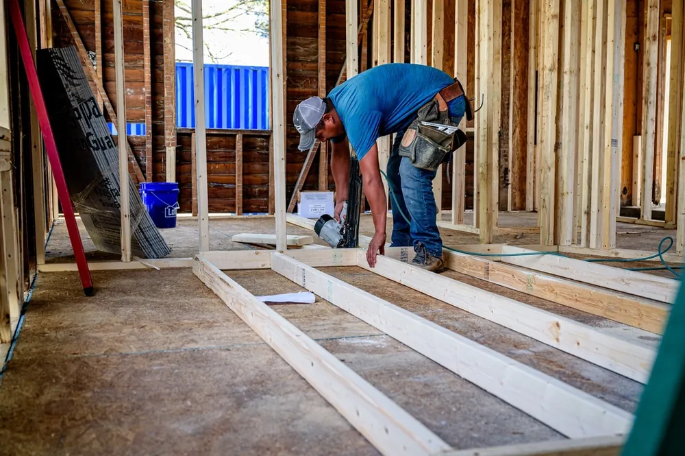 Builder measuring a floor frame inside a home under construction
