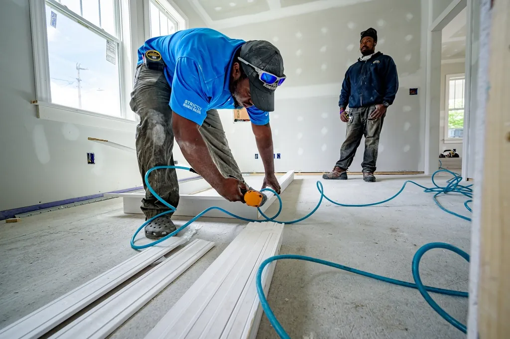 Builder fitting trim in a bright room while a colleague looks on