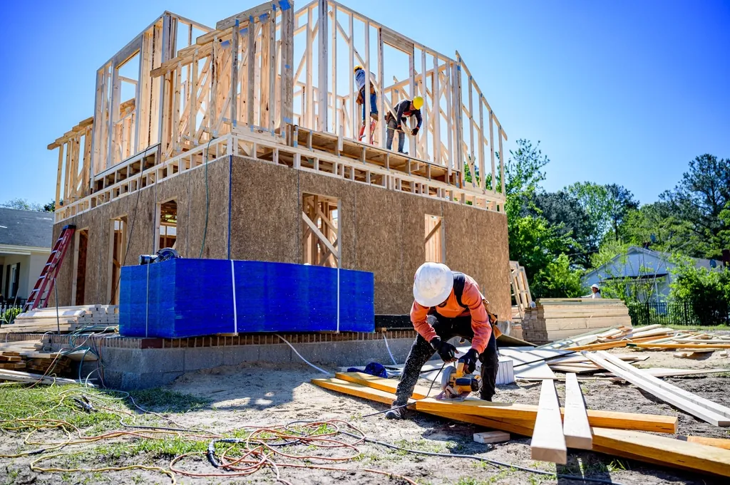 Crew working beside a two story wood frame house going up